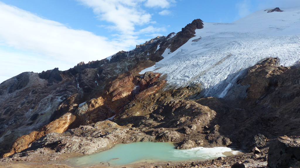 This December 2015 photograph shows the western flank of Volcán Cayambe with a small glacial lake (about 2 km down the SW flank), just above the Refugio Ruales Oleas Bergé. The presence of an ice cap at its summit represents a significant hazard, because melting of the ice by even small eruptions could generate large-volume lahars or debris flows. Photo by Ailsa Naismith, 2015.