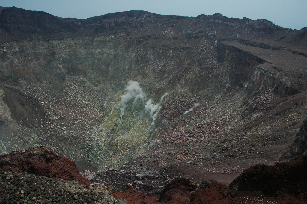The roughly 800-m-wide San Miguel crater is seen here in 2011 with fumaroles in the geothermal area on the far crater wall producing small gas-and-steam plumes. Different colors in the crater walls are from various levels of oxidation and geothermal alteration of the rock. Photo by Lis Gallant, 2011.
