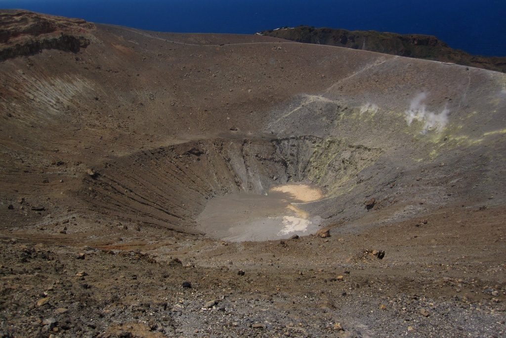 The summit crater of the Vulcano Fossa cone is seen here in May 2011. On the crater wall to the right is discoloration from geothermal activity consisting of fumaroles across a fracture zone. In 2010 the average measured temperature across the field was 190°C. Photo by Arianna Soldati, 2011.