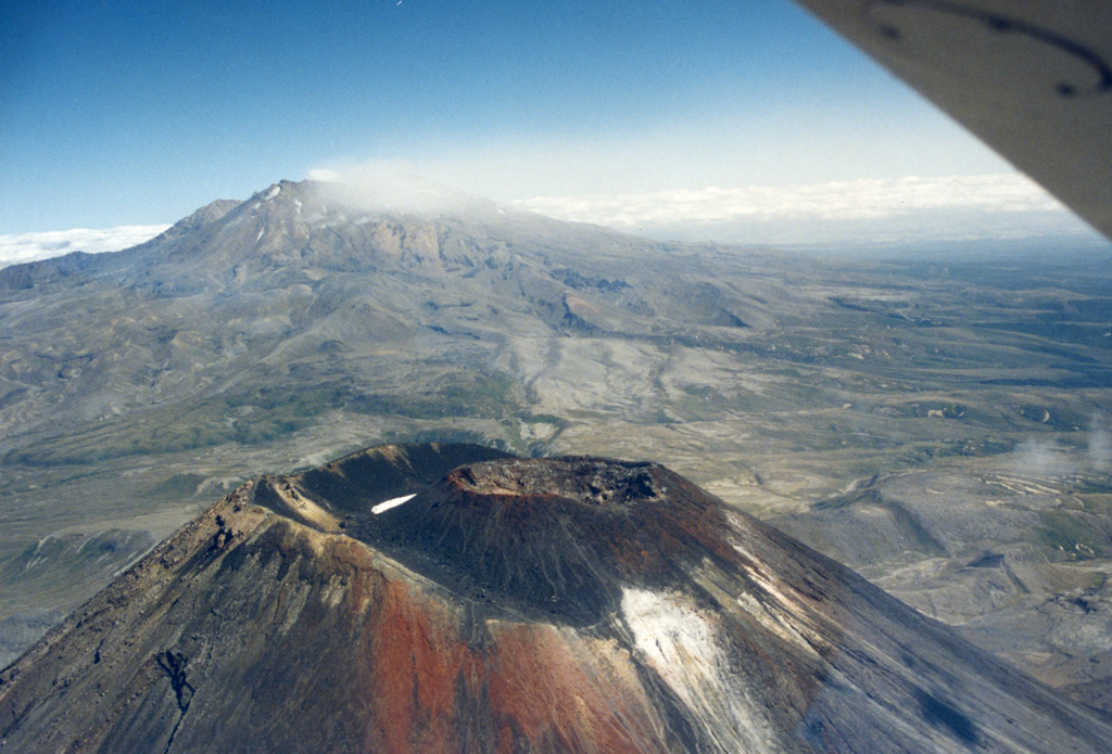 The Ngāuruhoe summit of the Tongariro volcanic complex is in the foreground, while in the background is a weak plume produced during the 1995-96 Ruapehu eruption, dispersing to the SW. The scoria cone within the Ngāuruhoe crater largely formed during the 1954-55 eruption and produced lava flows down the NW to W flanks. Photo by John A Krippner, 1995-1996.