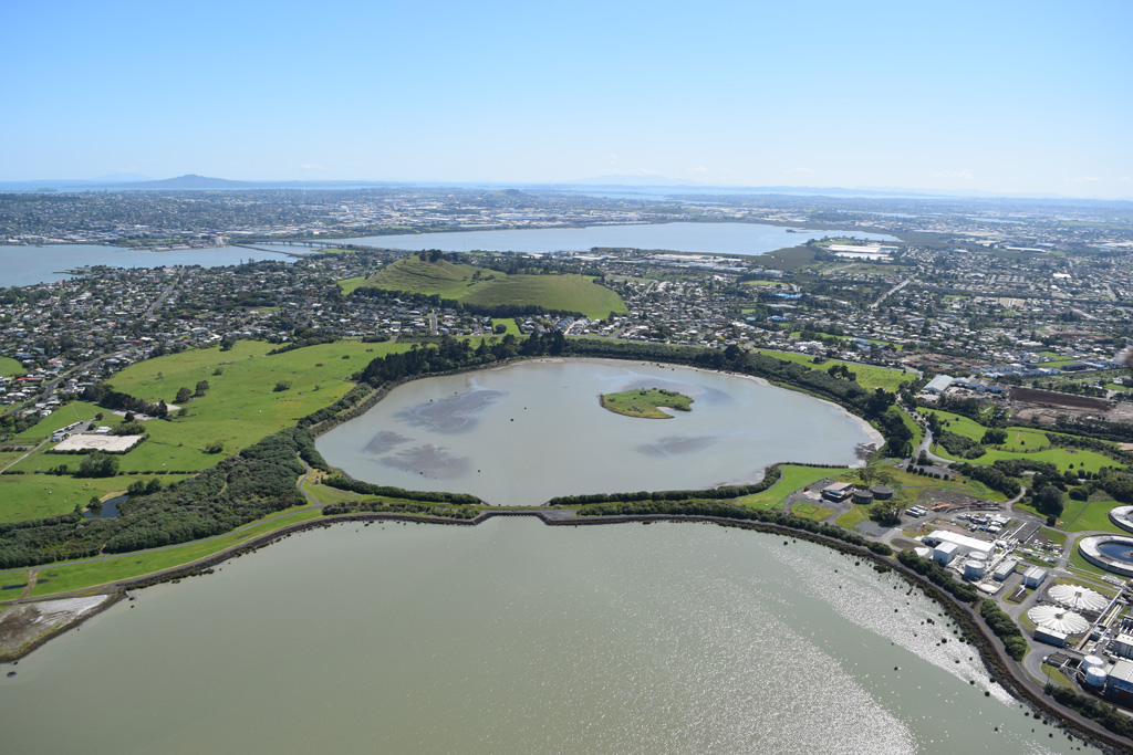Mangere Lagoon is a tuff ring that formed during a phreatomagmatic eruption in the Auckland Volcanic field. The activity has been linked to the Mangere scoria cone behind it (immediately to the upper left). Rangitoto is to the upper left of this 2018 view from the SW. Photo by Bruce Hayward, 2018.
