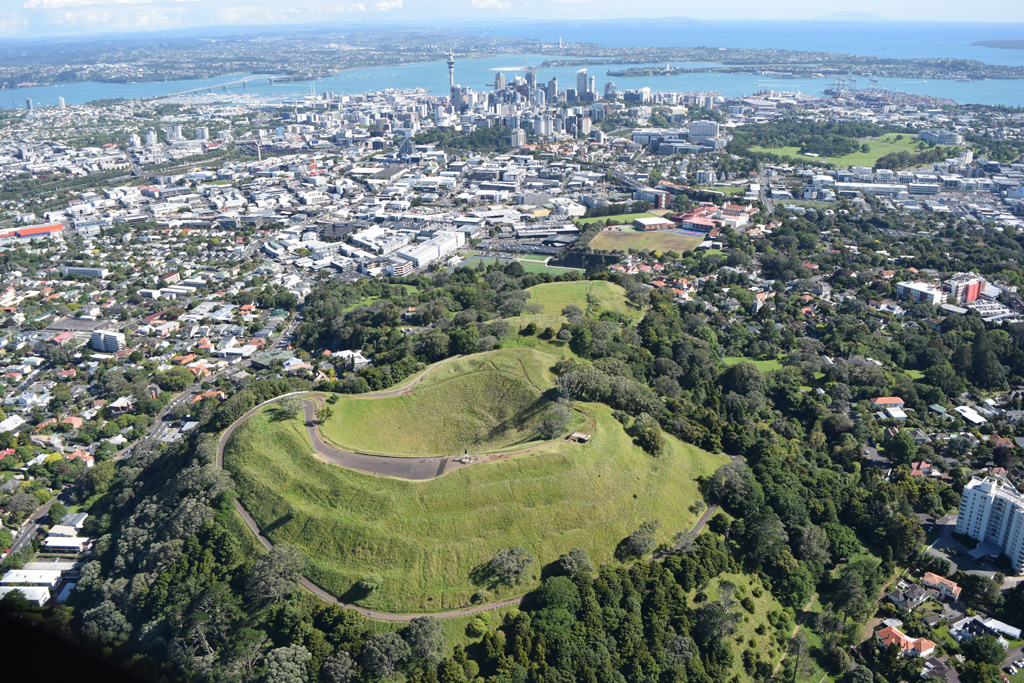 Maungawhau or Mount Eden is seen here in 2018 with the Auckland city center in the background. It is a scoria cone with a 50-m-deep crater and surrounding lava flows, and is one of around 50 vents within the Auckland Volcanic Field. Photo by Bruce Hayward, 2018.