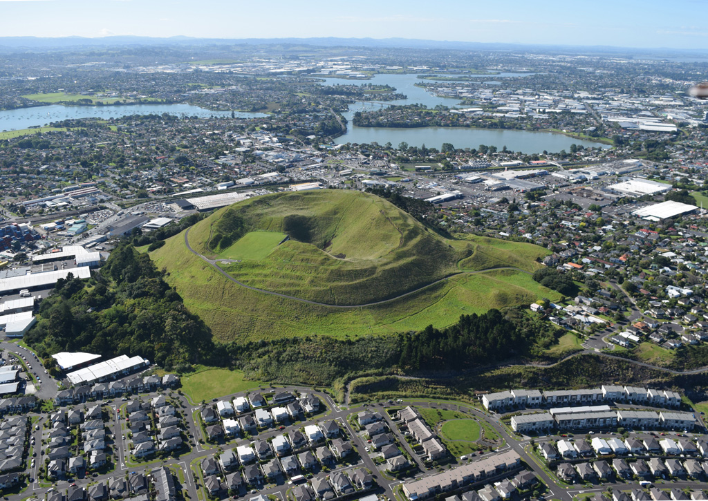 Mount Wellington or Maungarei is a scoria cone in the Auckland Volcanic Field with several summit craters that erupted around 10,000 years ago. This 2018 view from the NNW also shows the Panmure Basin or Te Kopua Kai-a-Hiku maar in the background. Photo by Bruce Hayward, 2018.