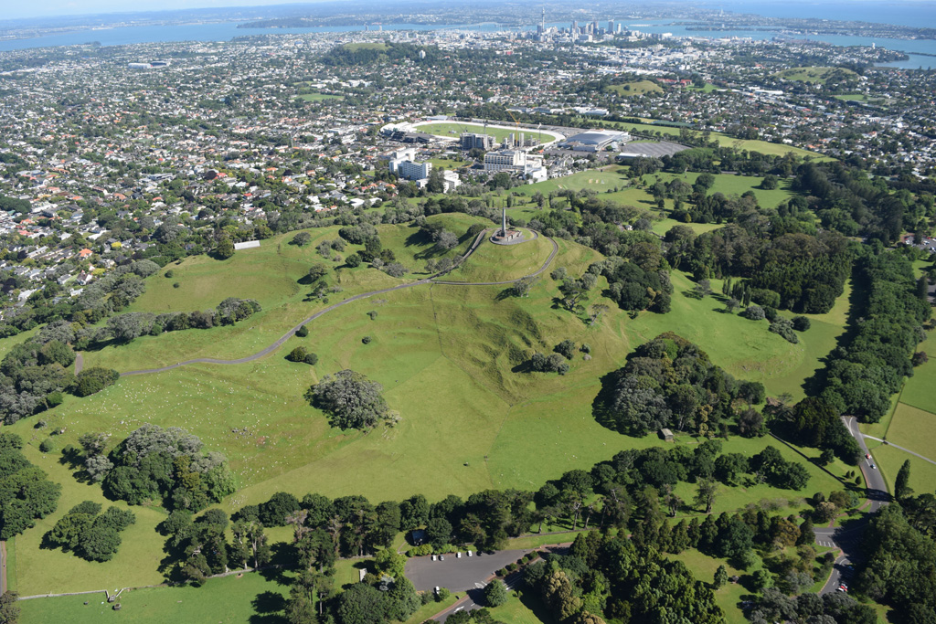 The One Tree Hill or Maungakiekie scoria cone has several summit craters and formed extensive lava flows during one of the larger eruptions of the Auckland Volcanic Field. This 2018 view is looking towards the SE with the Auckland city center in the background. Photo by Bruce Hayward, 2018.