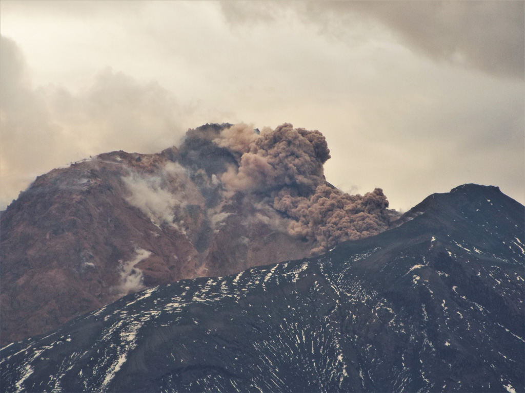 An avalanche descends the NE flank of the Sheveluch lava dome on 6 July 2015, seen above the 1964 flank collapse scarp rim. Fragmentation of the hot dome rock produces the beginning of an ash plume above it and degassing is also visible across the dome. Photo by Janine Krippner, 2015.