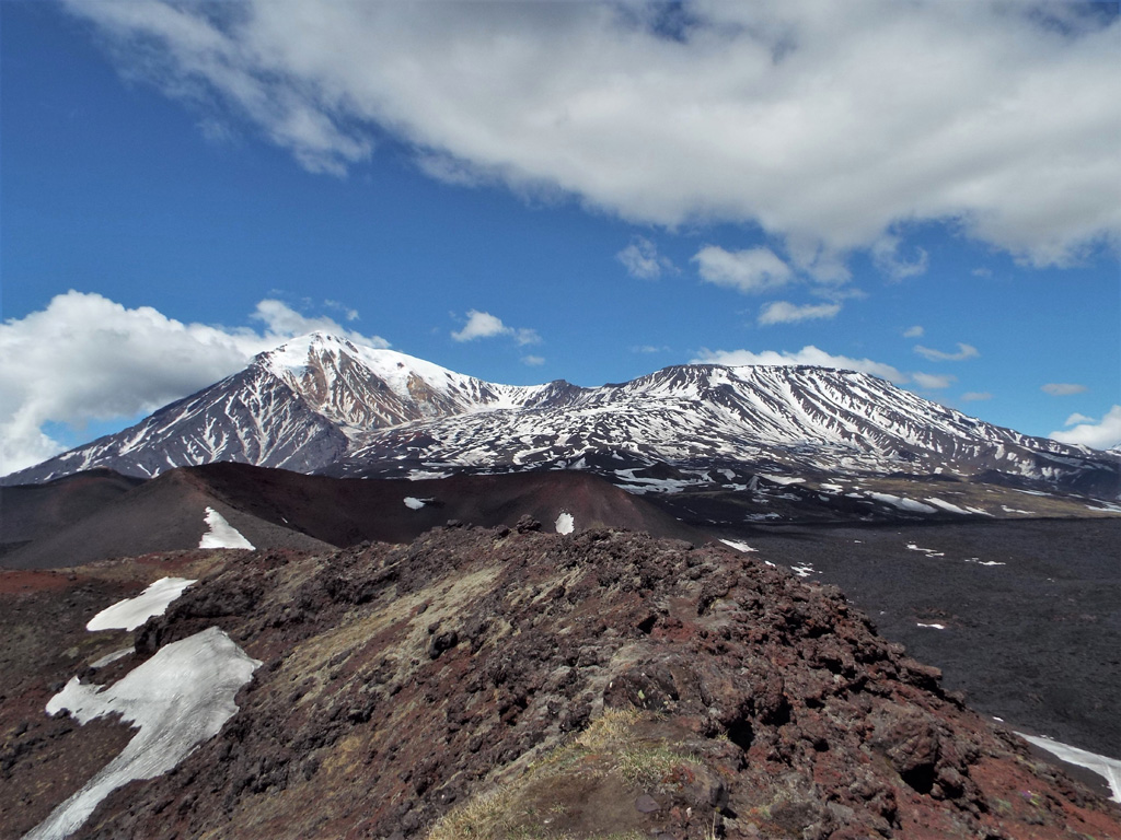 The main Tolbachik edifice is seen here from one of the southern flank scoria cones, with the Ostry peak to the left and the broader Plosky to the right. The 2012-13 lava flow is to the lower right of the scoria cones. Photo by Janine Krippner, 2015.