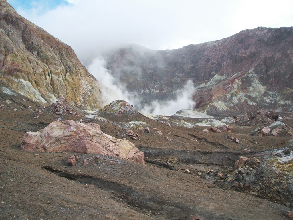 This photo looks towards the western crater lake at Whakaari/White Island, which is emitting volcanic gases and steam. The crater walls expose lavas and tuff deposits, and across the central crater floor (foreground) are blocks and hummocks of the 1912 debris avalanche deposit. Photo by Janine Krippner, 2005.