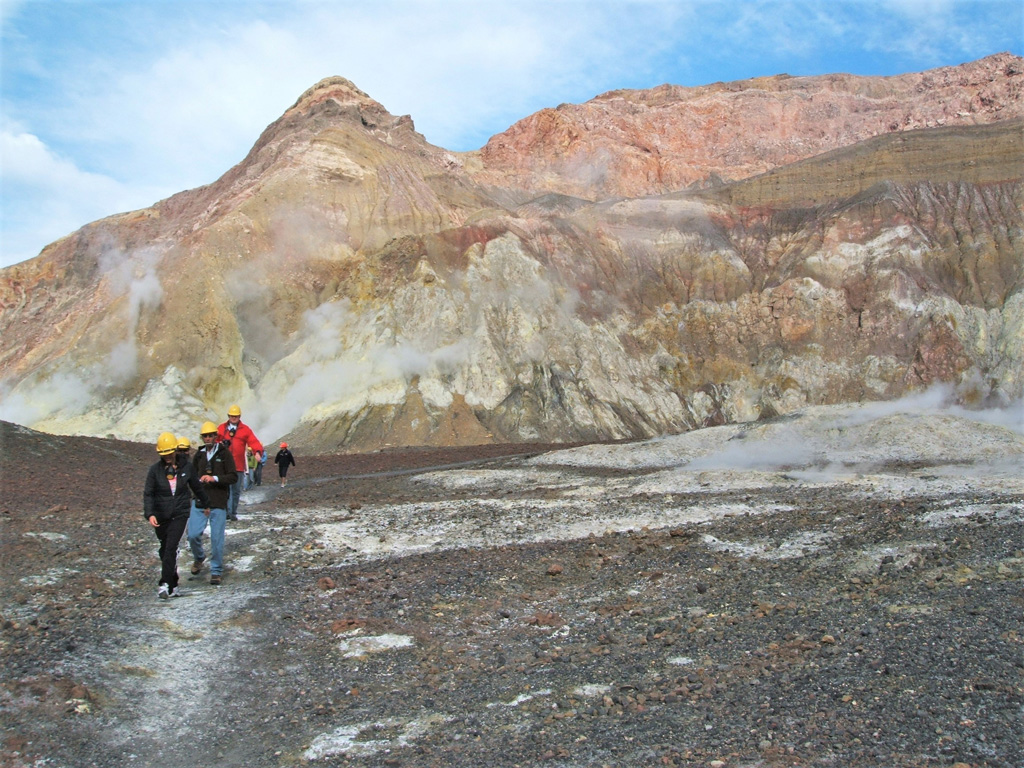 Tourists walk across the Whakaari/White Island crater floor in August 2005. The crater wall behind them is composed of lavas, breccias, and tuff deposits. Photo by Janine Krippner, 2005.
