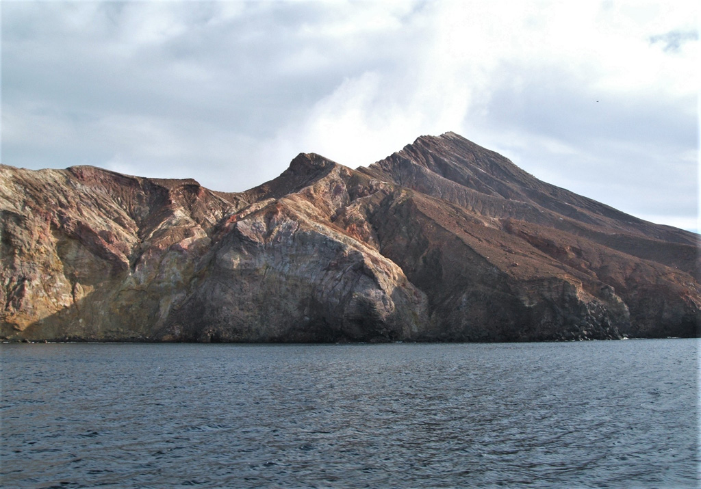 This 22 August 2005 photo shows the E side of the Whakaari/White Island Central Cone showing the exposed stratigraphy of tuff, lava, and breccia units. The gas-and-steam plume rising from the active vent is visible above the flank. Photo by Janine Krippner, 2005.